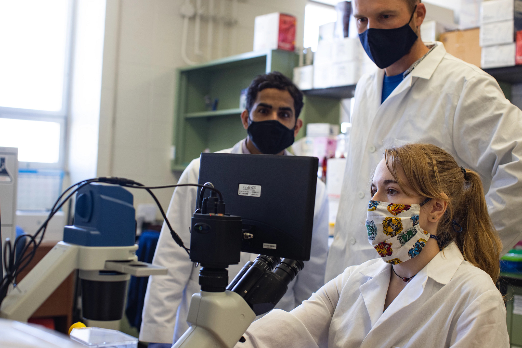 3 people standing around a computer screen with microscope